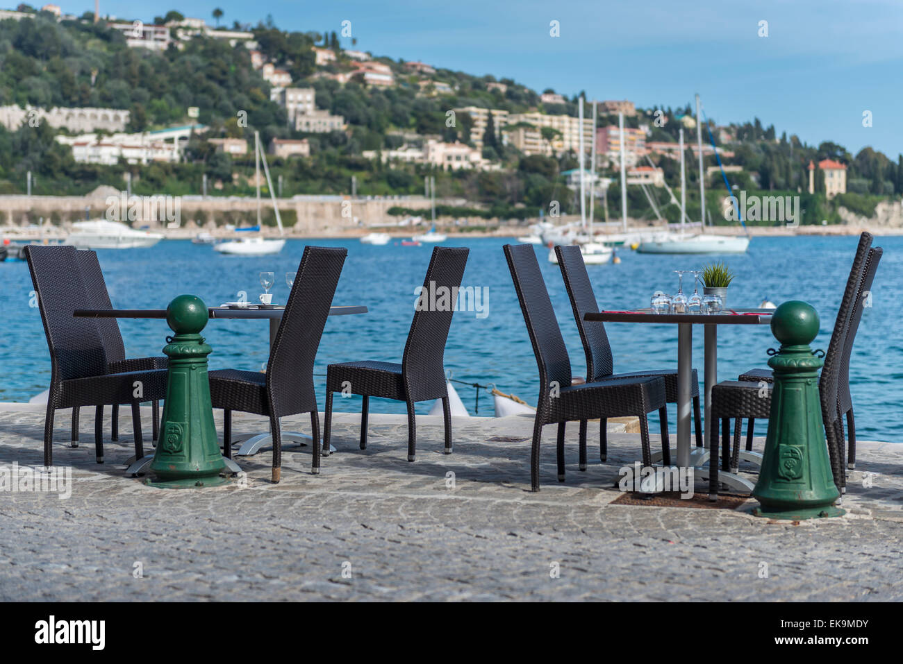 A pair of bistro tables on the harbour edge with yachts in the ...