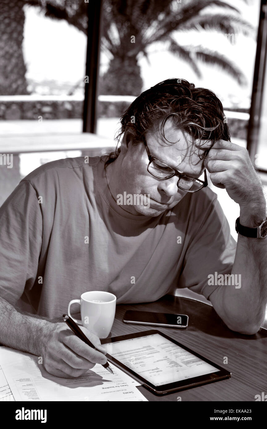 B&W Mature man in holiday setting concentrating on financial statements and business papers along with his iPad Air and iPhone 6 Stock Photo