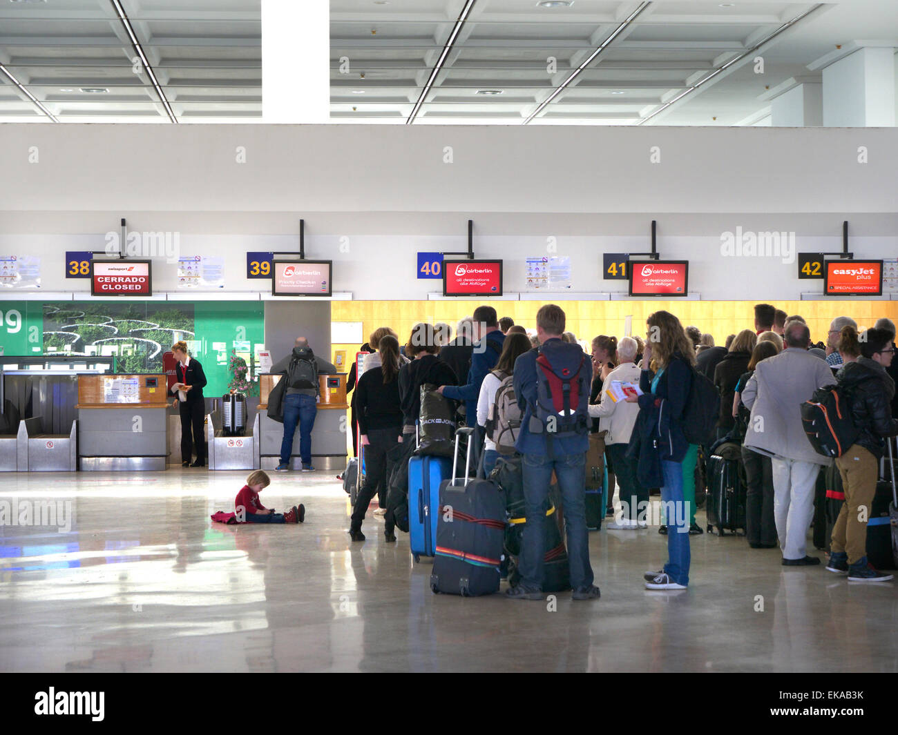 Lines of charter flight passengers and luggage wait at airport terminal to check in to their flight Stock Photo