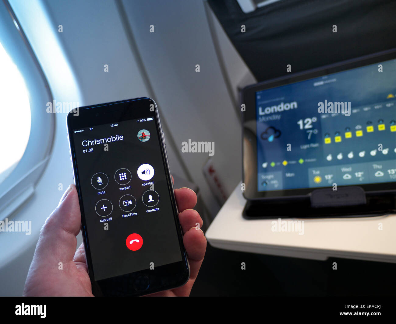Hand holding iPhone 6 smartphone calling in-flight with iPad air tablet computer screen displaying current weather in London UK Stock Photo