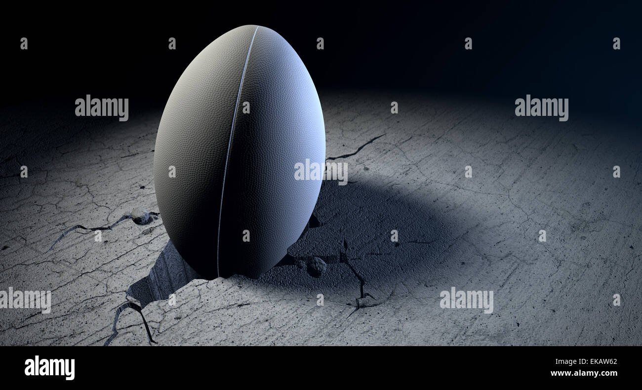 A white dimpled rugby ball stuck in a whole cracked in the ground on a ...