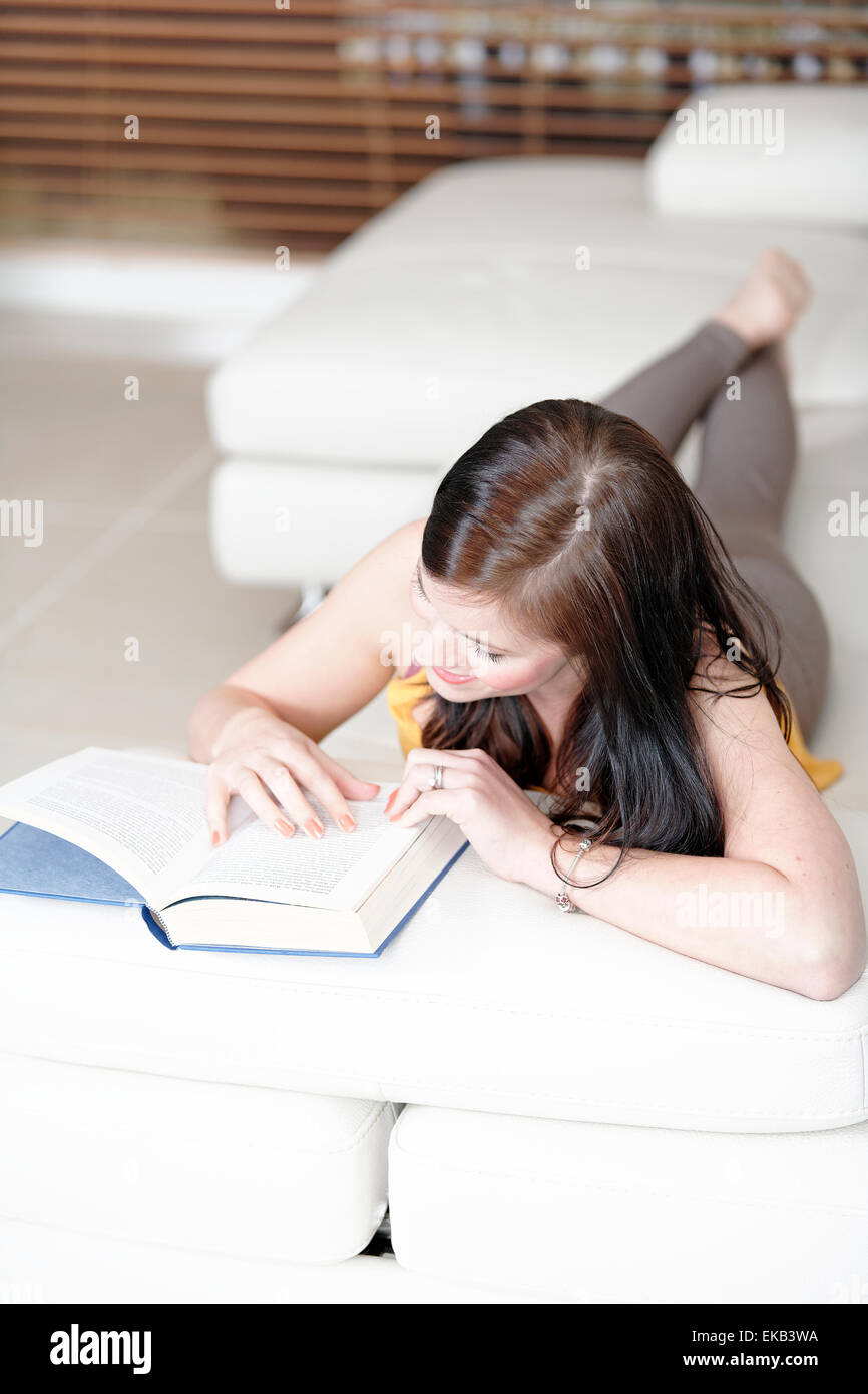 Woman lying on sofa with a book Stock Photo - Alamy