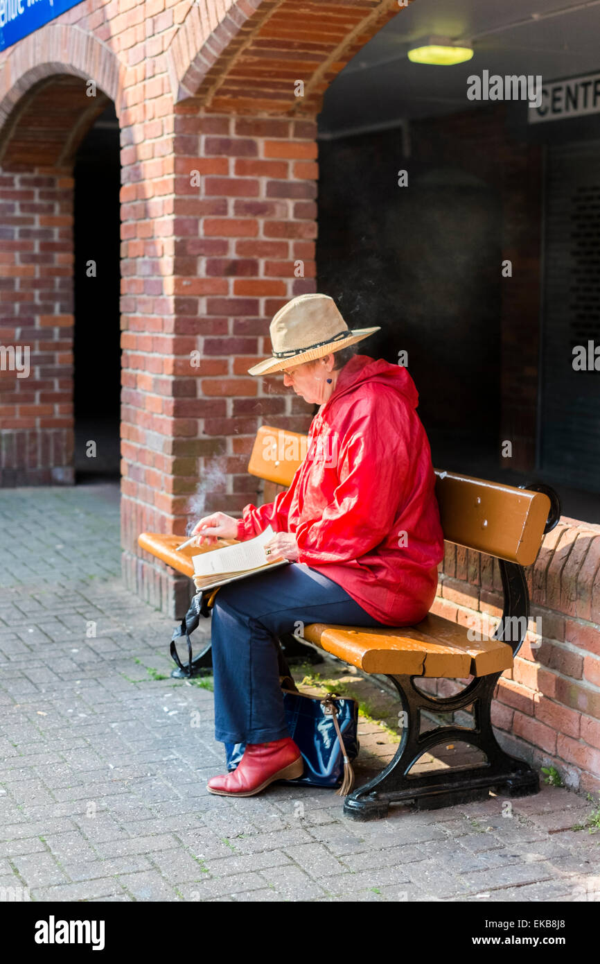 Old lady sat reading a book whilst smoking Stock Photo