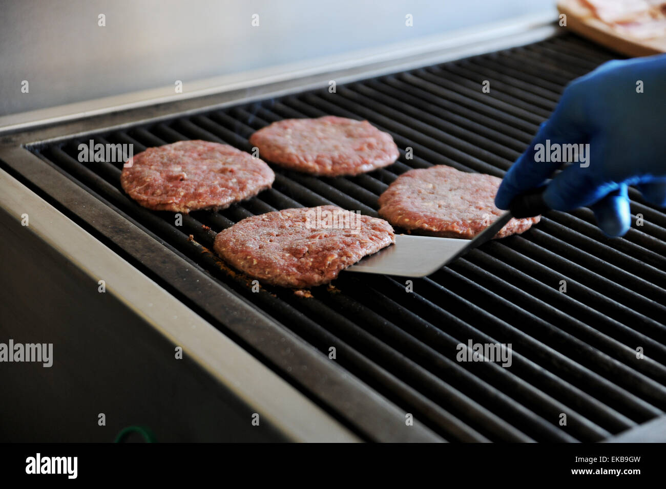 Freshly made beef burgers cooking on a hot griddle at a fast food take