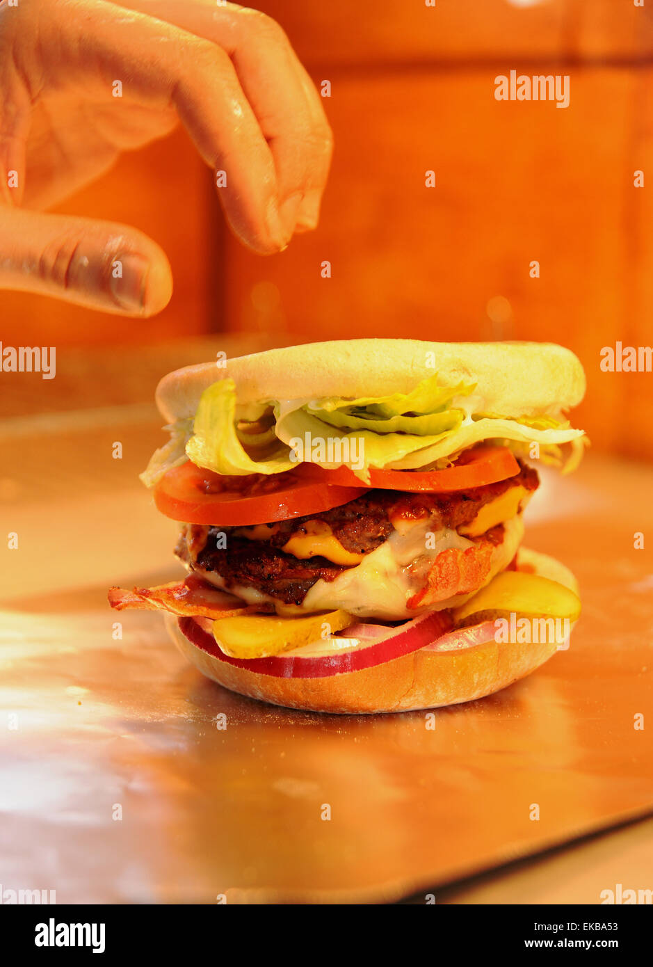 Burger in a bun with cheese and bacon in the hot service area of take away fast food shop Stock Photo