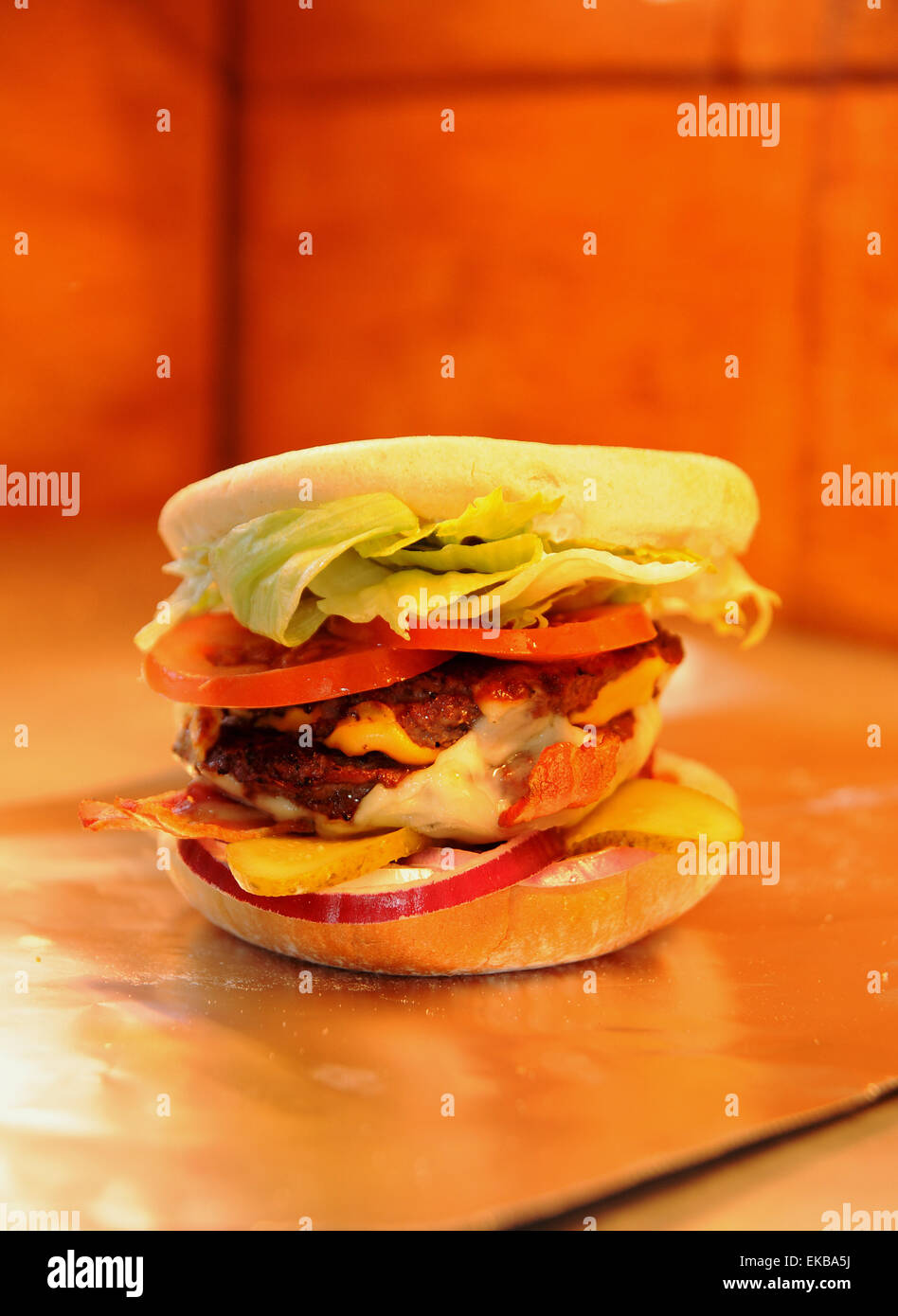 Burger in a bun with cheese and bacon in the hot service area of take away fast food shop Stock Photo