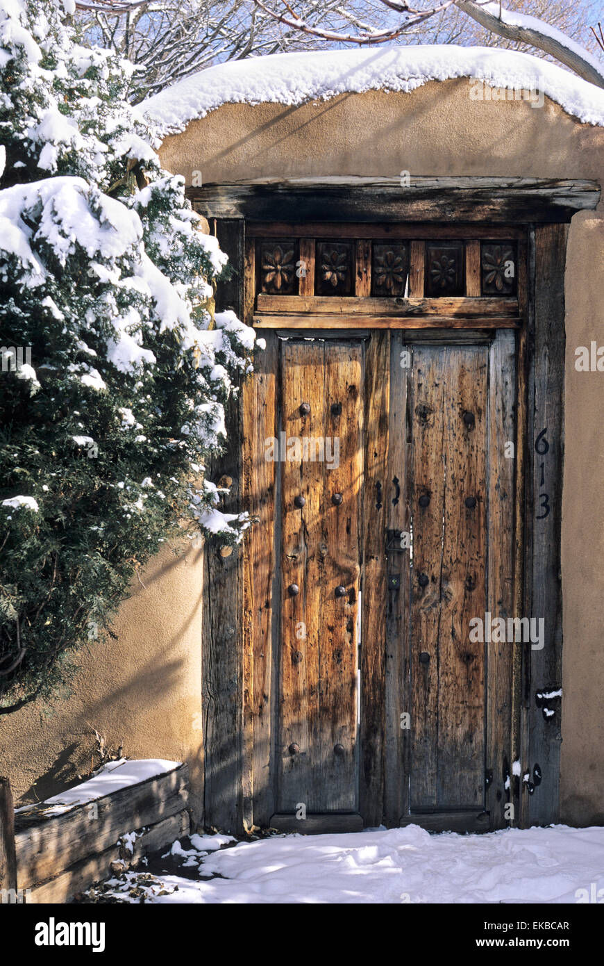 A wooden gate set into an adobe wall seems to take on a ronamtic air when covered with a dusting of winter snow. Stock Photo