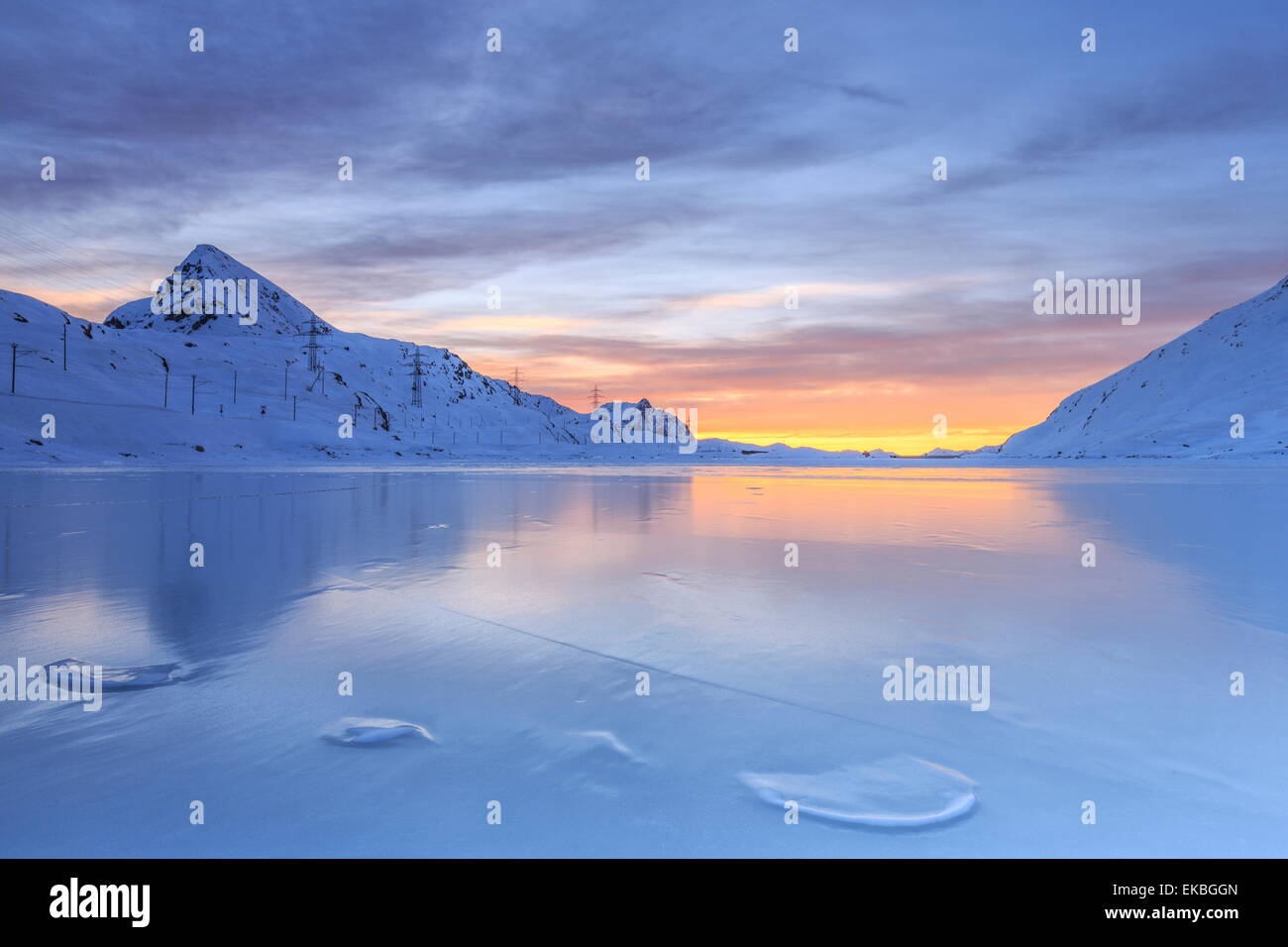 The colors of dawn invading the smooth surface of Lago Bianco, Bernina Pass, Graubunden, Swiss Alps, Switzerland Stock Photo