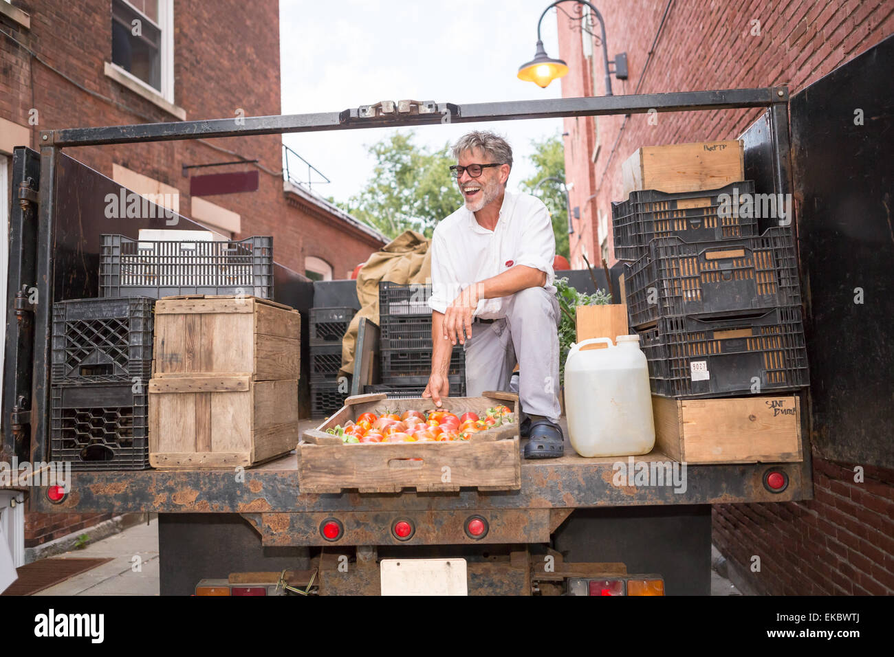 Farmer unloading crates of organic tomatoes outside grocery store Stock Photo