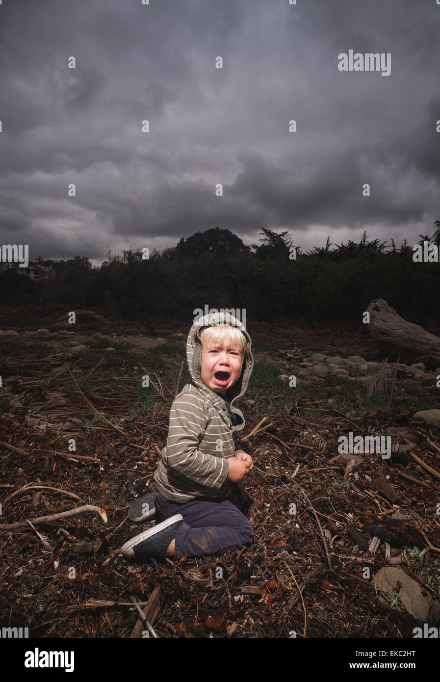 Young boy kneeling on ground crying against stormy sky Stock Photo