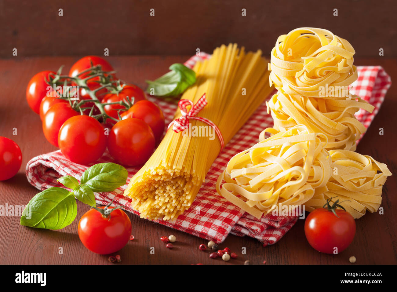 raw spaghetti pasta basil tomatoes. italian cuisine in rustic kitchen Stock Photo