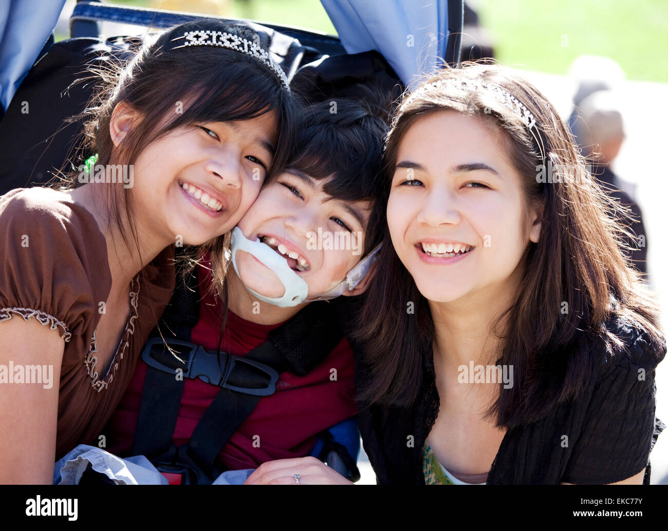 Disabled boy in wheelchair surrounded by big sisters, smiling Stock Photo