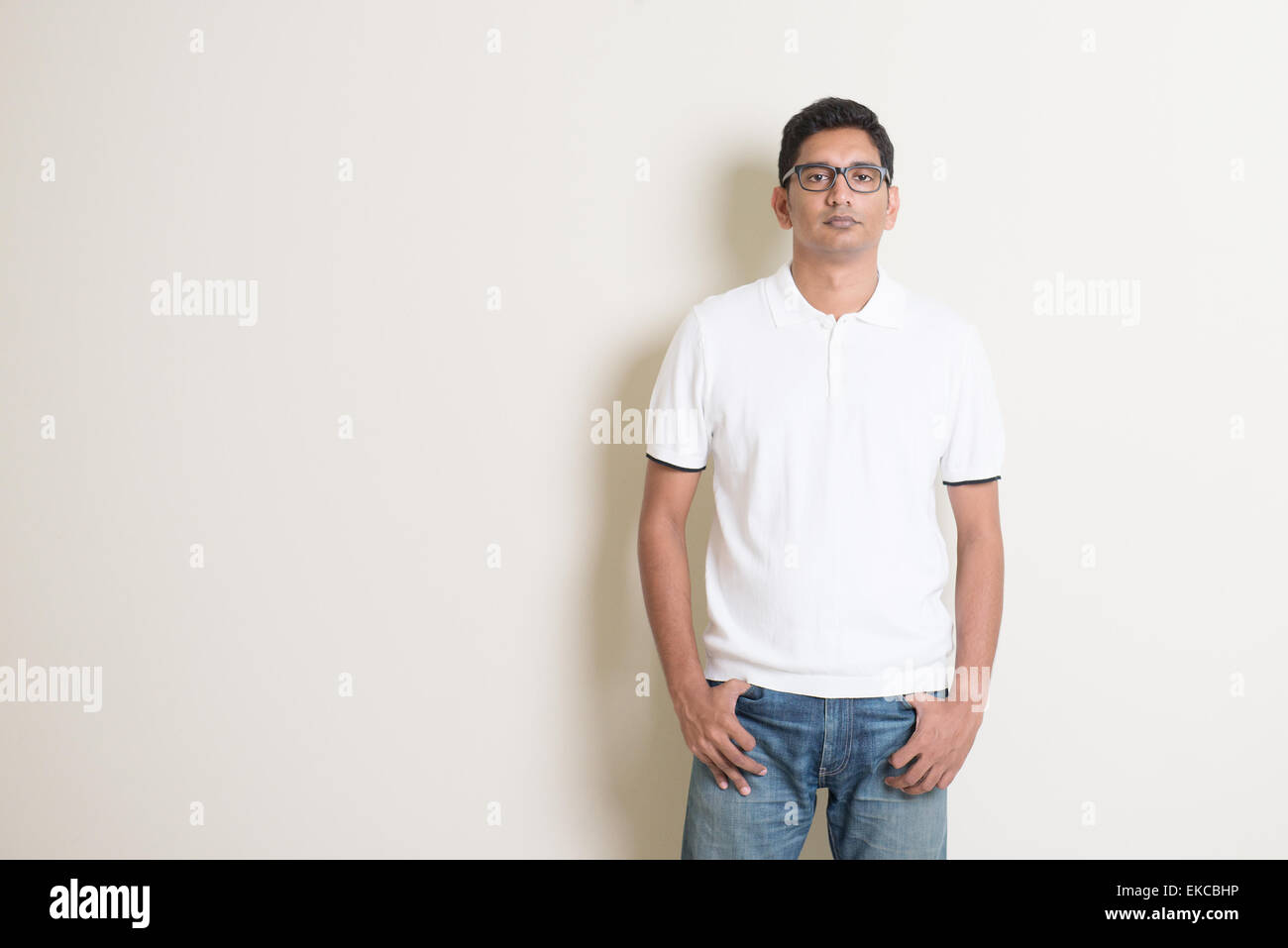 Portrait of cool Indian guy looking at camera, standing on plain background with shadow, copy space at side. Stock Photo