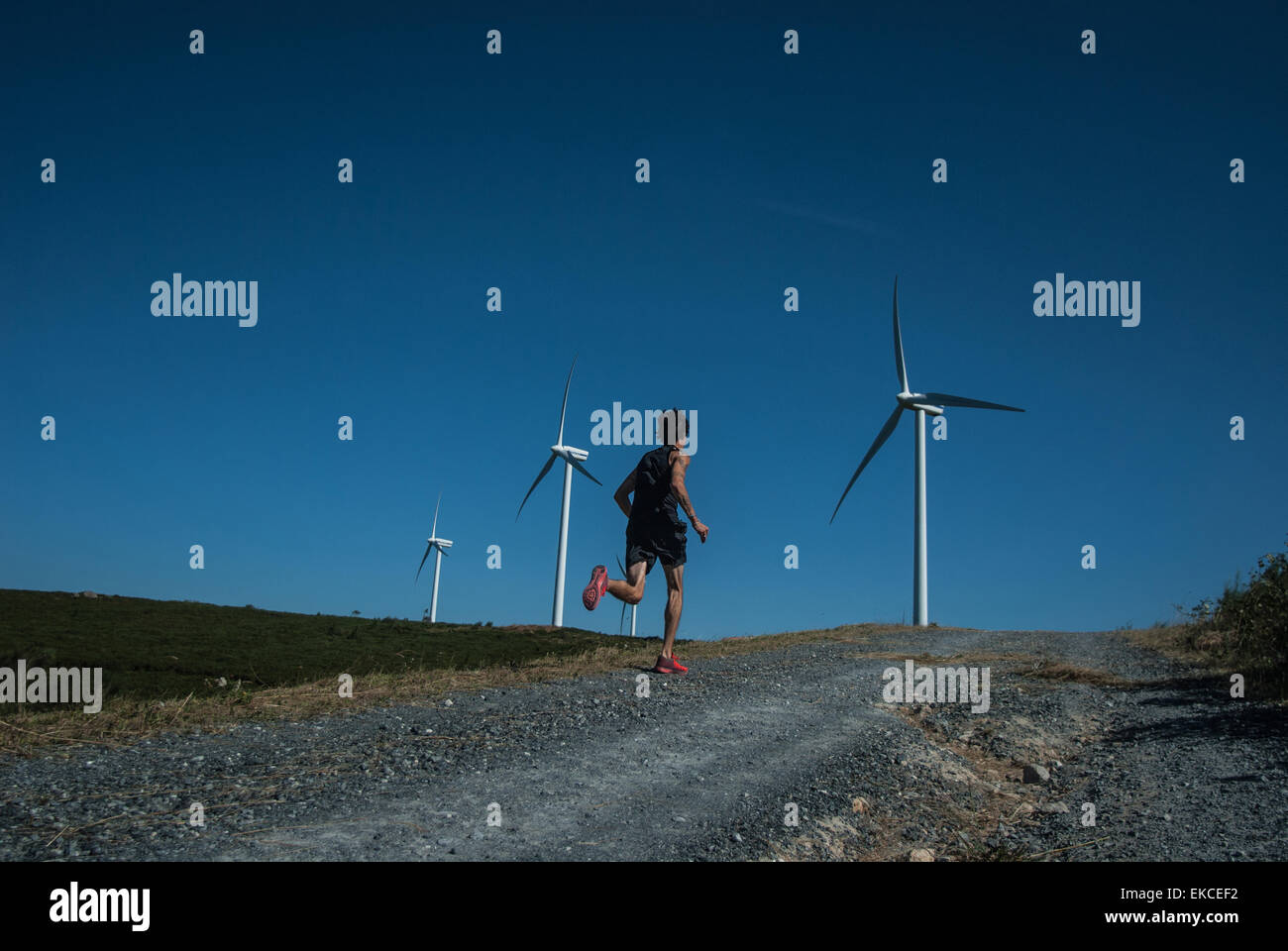 Mid adult man jogging on road, wind turbines in distance Stock Photo