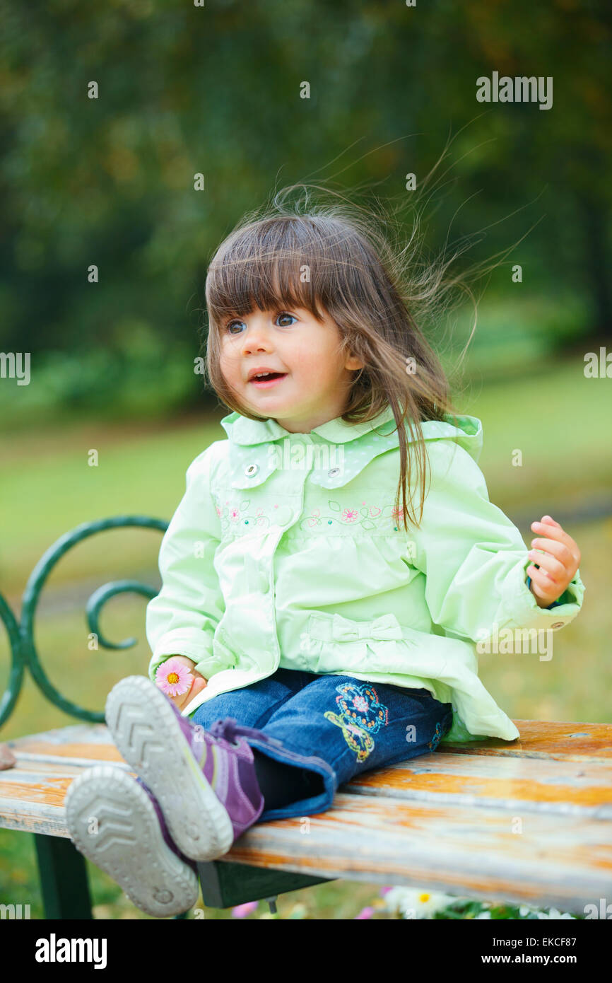 Little girl sitting on a bench in the park Stock Photo - Alamy