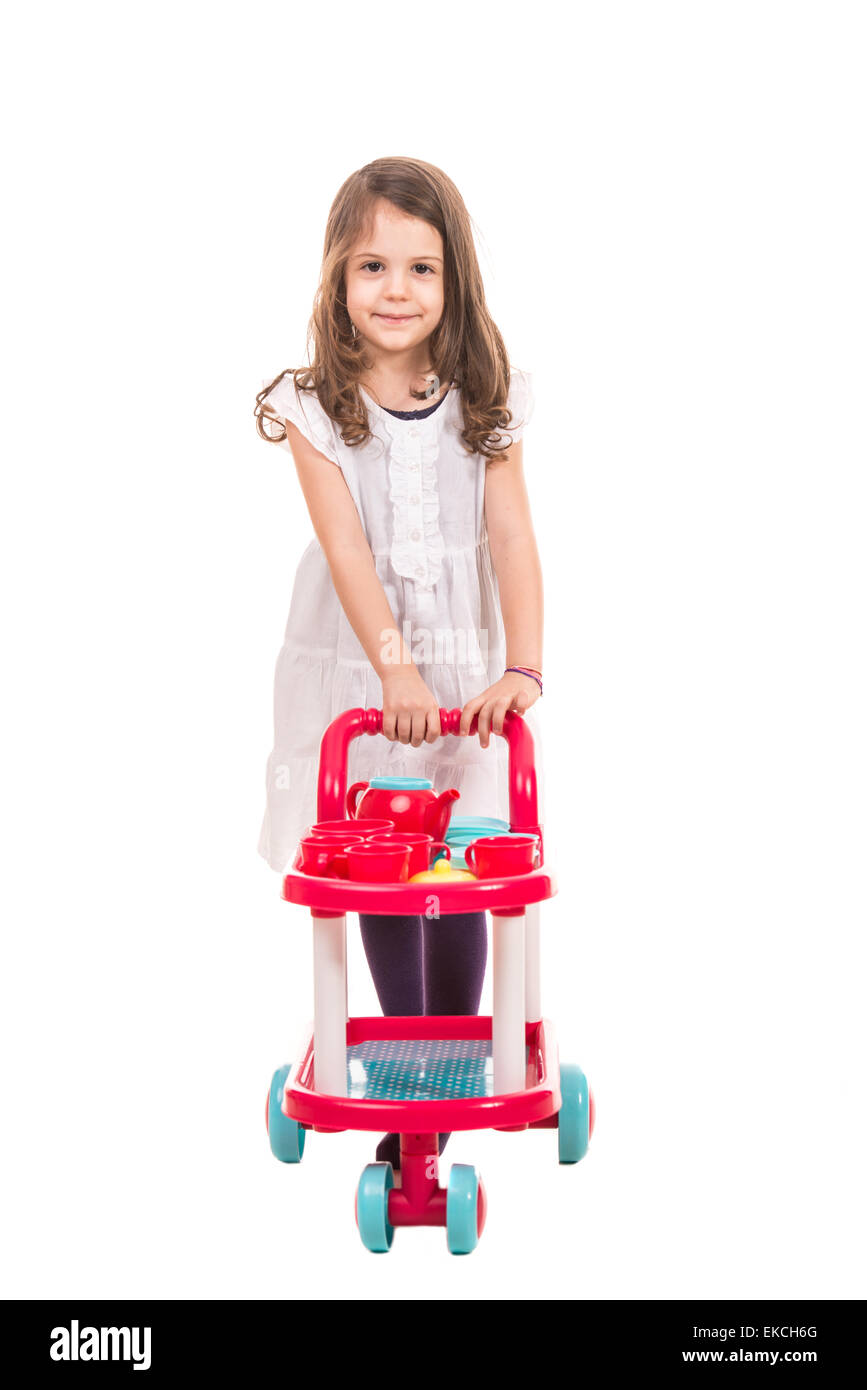 Little girl playing waiter and  pushing trolley pram with cups and kettle isolated on white background Stock Photo