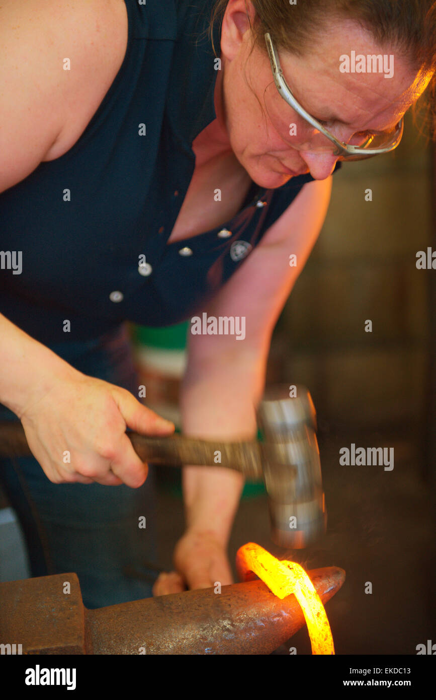 Woman farrier forging horseshoe on anvil Stock Photo