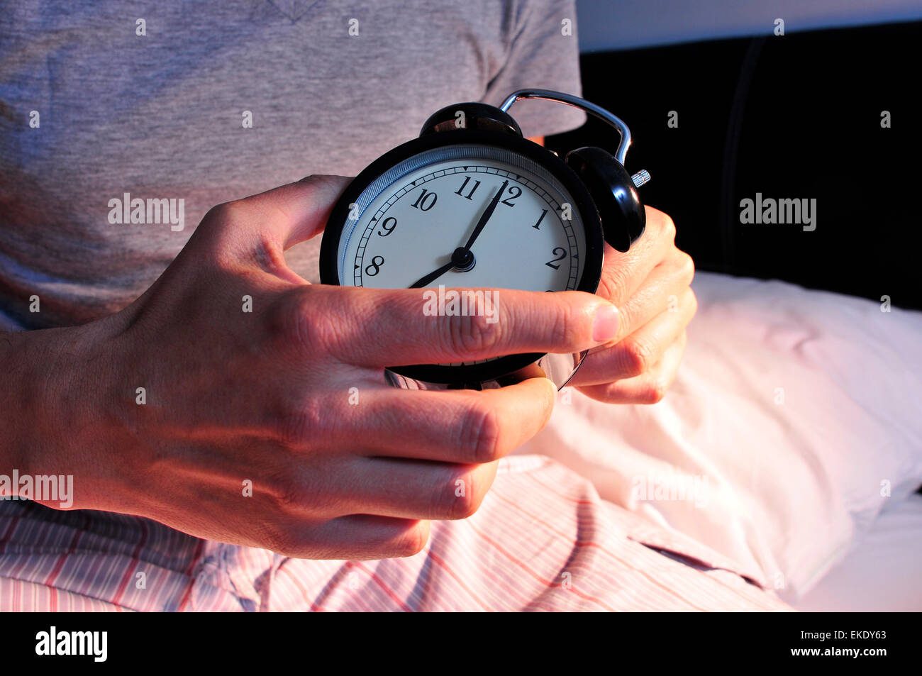 a young caucasian man wearing pajamas in bed setting the alarm clock at 7 before lie down Stock Photo