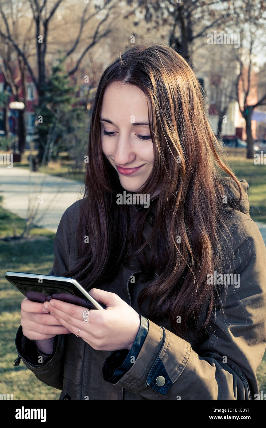 Pretty young teen girl smiling while holding tablet pc in her hands. Toned colorized image. Stock Photo