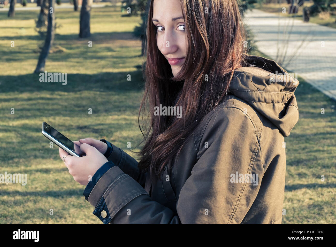 Young girl posing outdoors with tablet PC in her hands and look back. Toned colorized image, film like color. Stock Photo