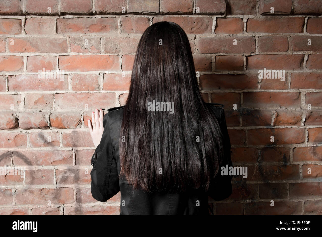 Rear view of a woman with long brown hair against red brick background Stock Photo