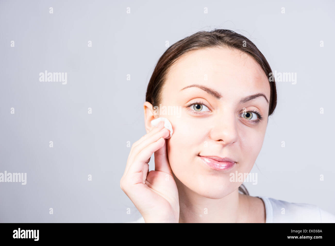 Close up Portrait of a Smiling Young Woman Scrubbing her Face Using a Cotton with Facial Cleanser While Looking at the Camera. C Stock Photo