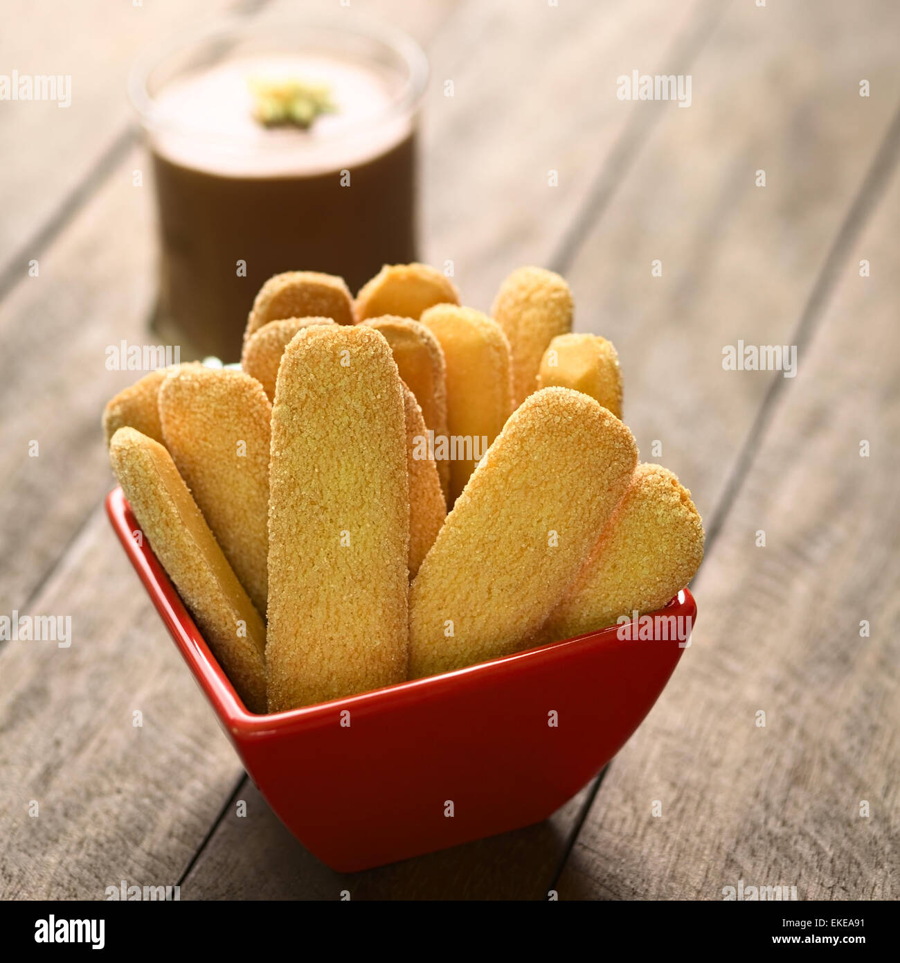 Ladyfinger biscuits in red bowl with chocolate mousse in the back