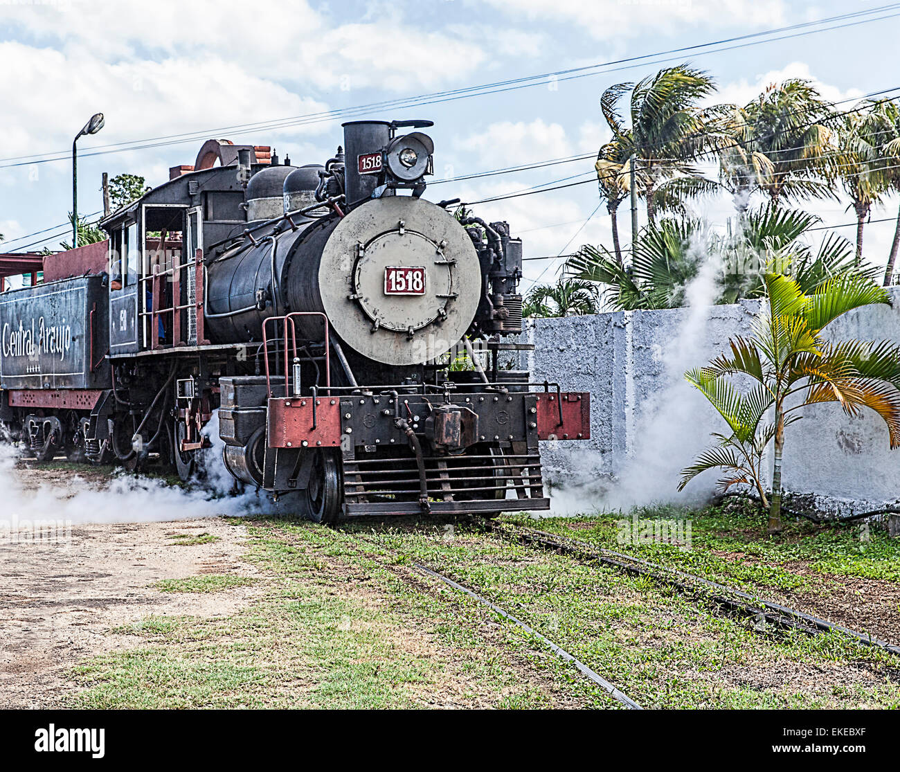 Restored old American steam train in Cuba with railway track and palm trees and dramatic cloudy sky. Stock Photo