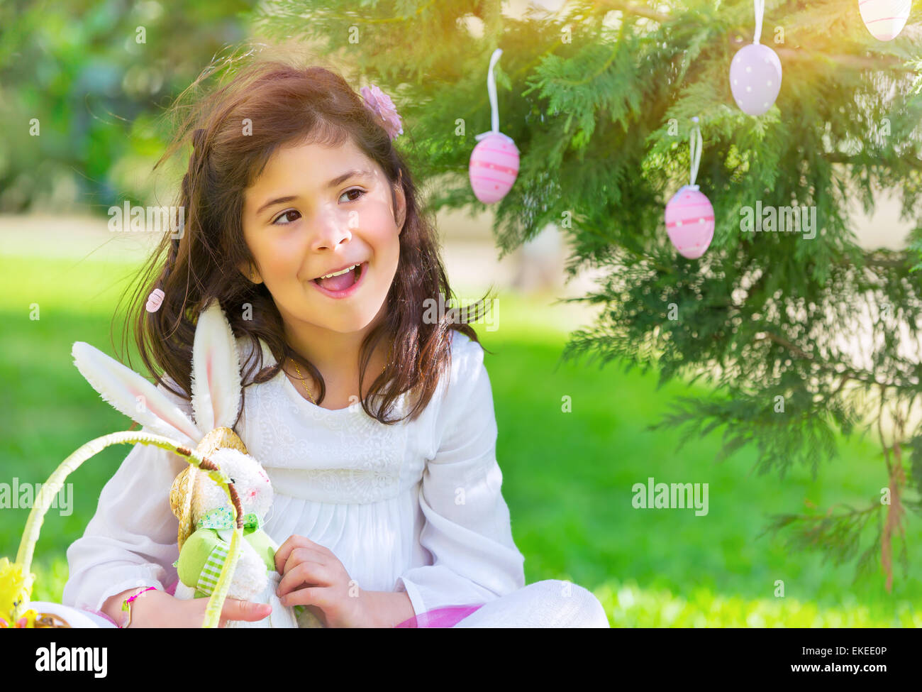 Portrait of nice little girl playing traditional Easter game, happy egg hunting, having fun at spring park in religious holiday Stock Photo