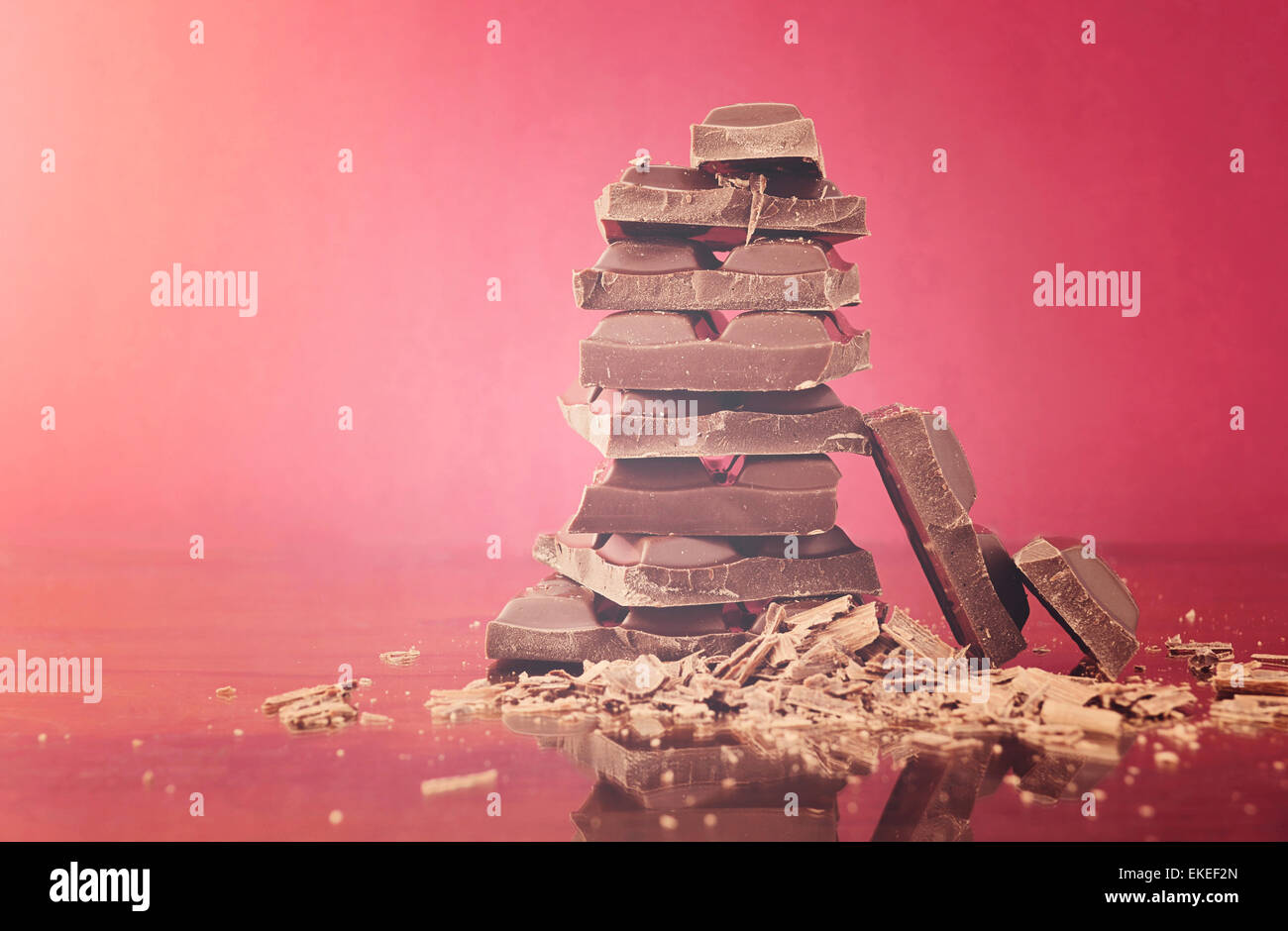 Stack of chocolate on reflective glass against red background with applied retro vintage style filters and added light flare. Stock Photo