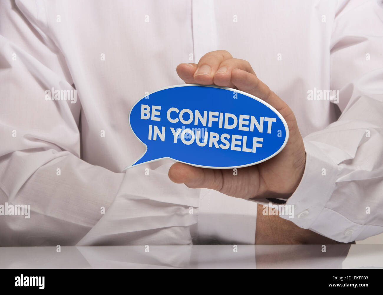 Image of a man hand holding blue speech balloon with the text be confident in yourself, white shirt and reflexion. Concept and m Stock Photo
