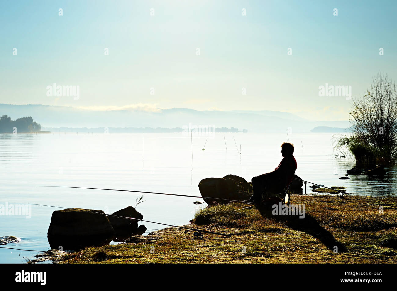 Silhouette of a fisherman on the lake at sunrise Stock Photo - Alamy