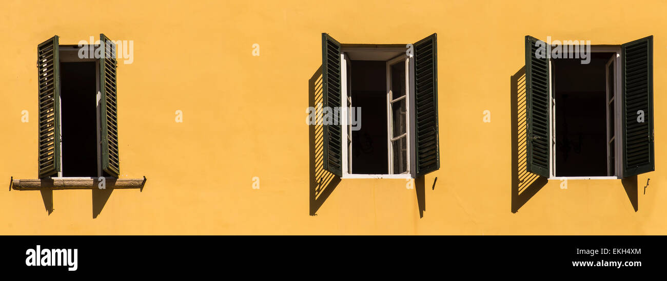 Three open windows with green shutters against yellow wall in Lucca, Tuscany, Italy Stock Photo