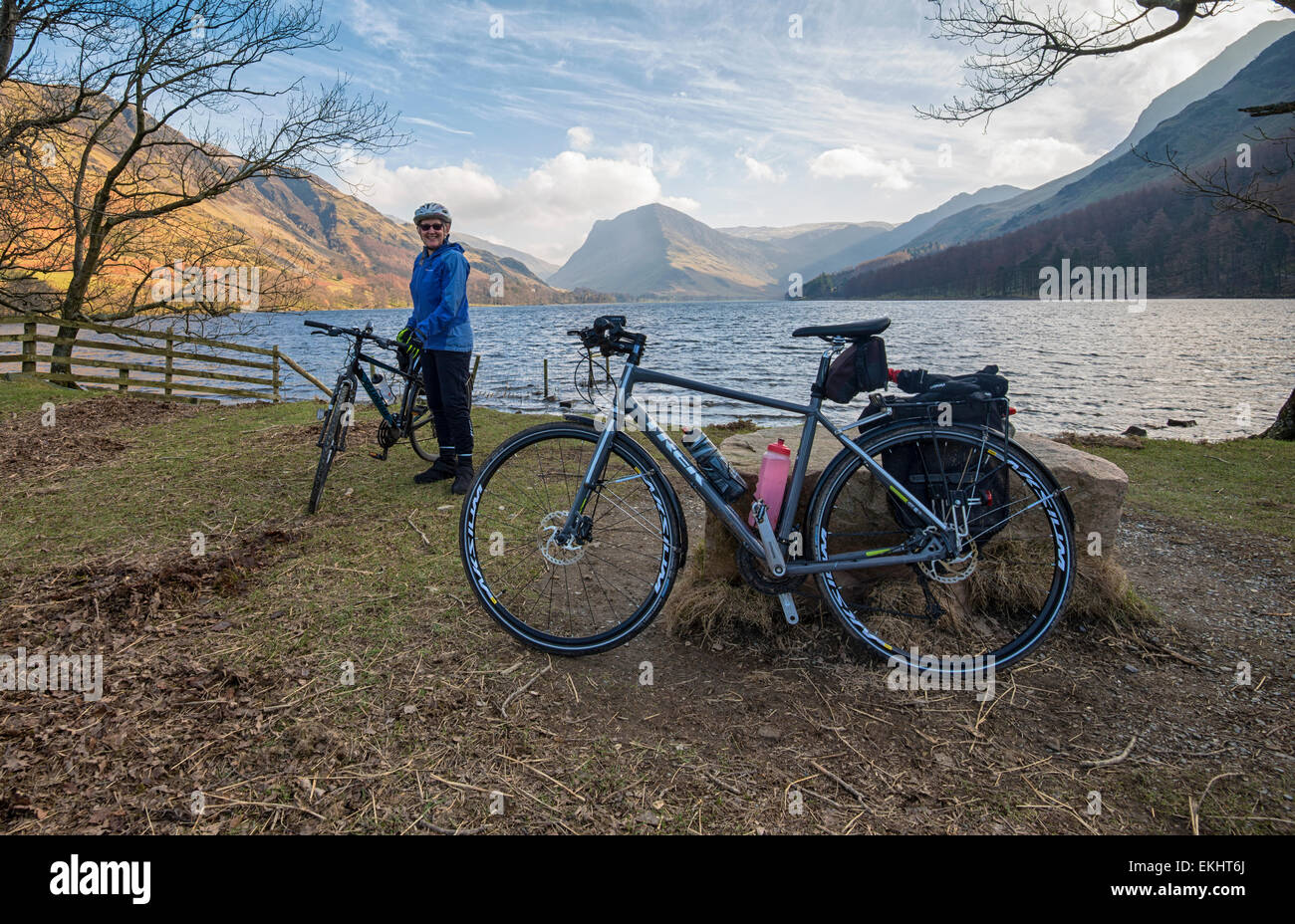 A female cyclist posing with hers and another bike in front of Loweswater in Cumbria, England Stock Photo