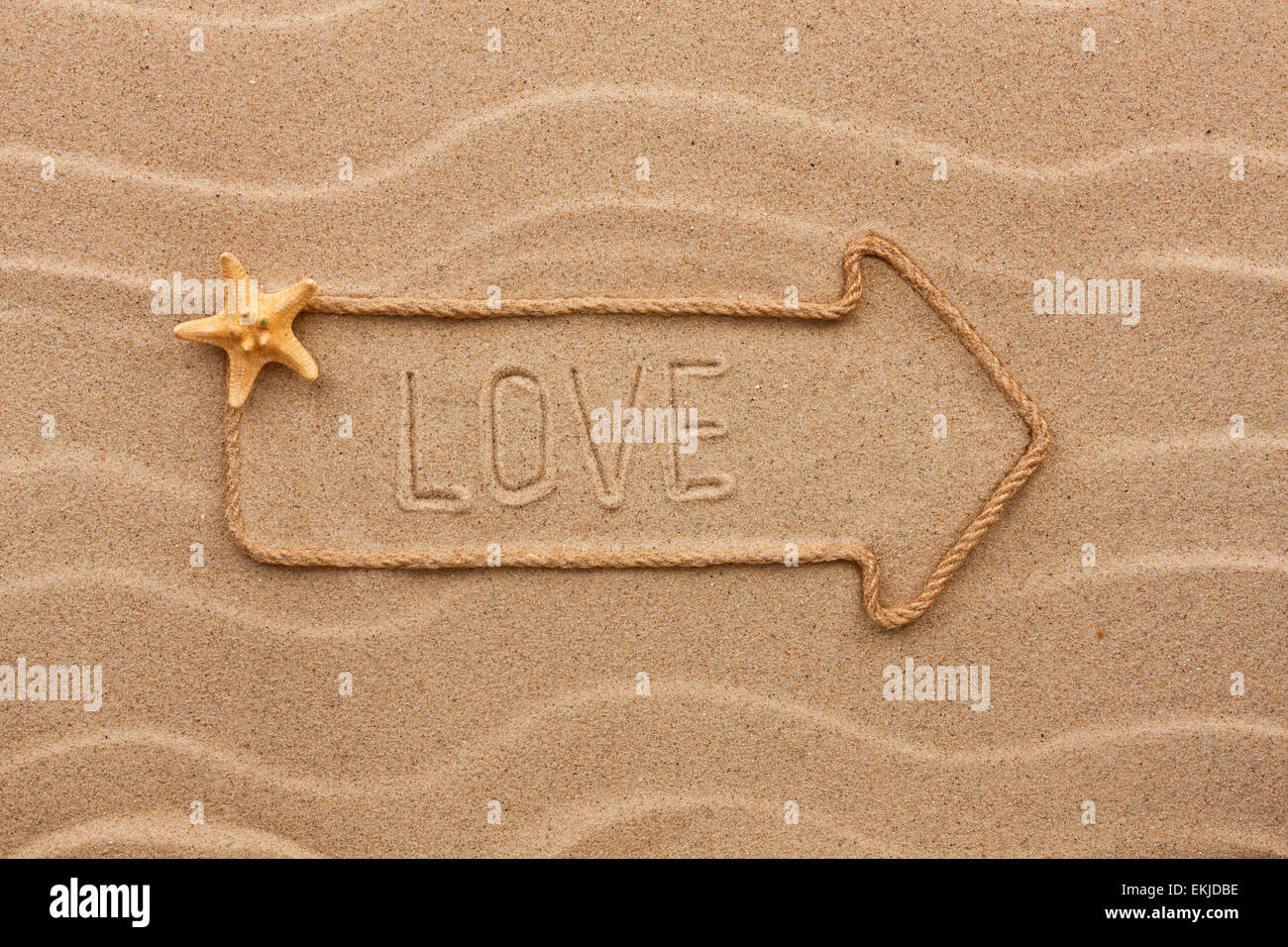 Pointer made of rope with an inscription  love, with starfish, on sand Stock Photo