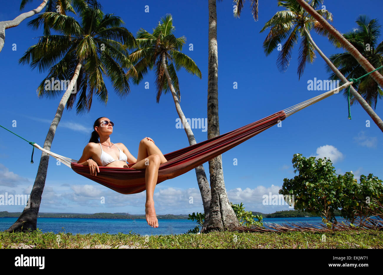Young woman in bikini sitting in a hammock between palm trees, Ofu island, Vavau group, Tonga Stock Photo