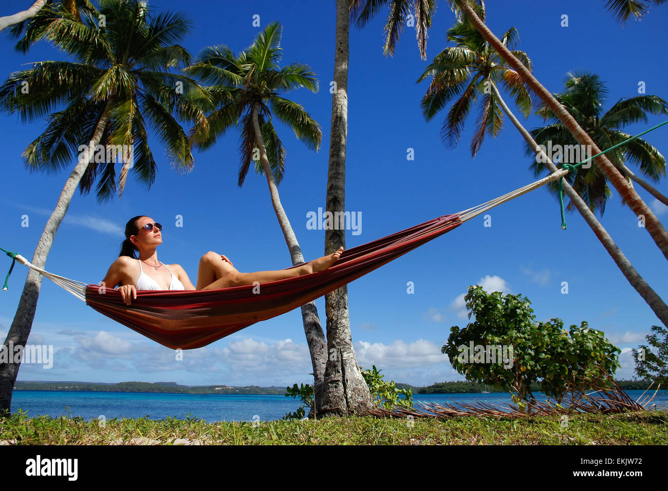 Young woman in bikini sitting in a hammock between palm trees, Ofu island, Vavau group, Tonga Stock Photo