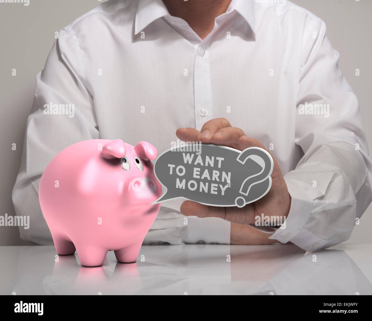 Image of a man hand holding speech balloon with the text want to earn money and pink piggy bank, white shirt. Concept for money Stock Photo