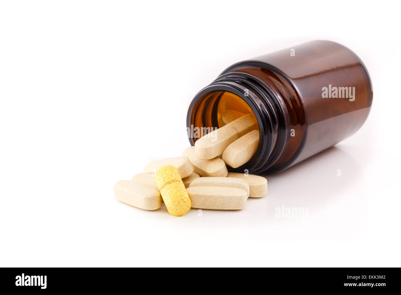 Pills fallen out of brown bottle. One pill is yellow and different. Studio shot on white background, view side of bottle. Stock Photo