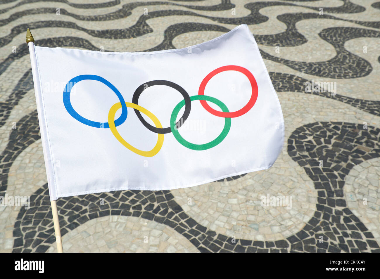 RIO DE JANEIRO, BRAZIL - FEBRUARY 23, 2015: Olympic flag waves in front of the iconic wave pattern of the Copacabana sidewalk. Stock Photo
