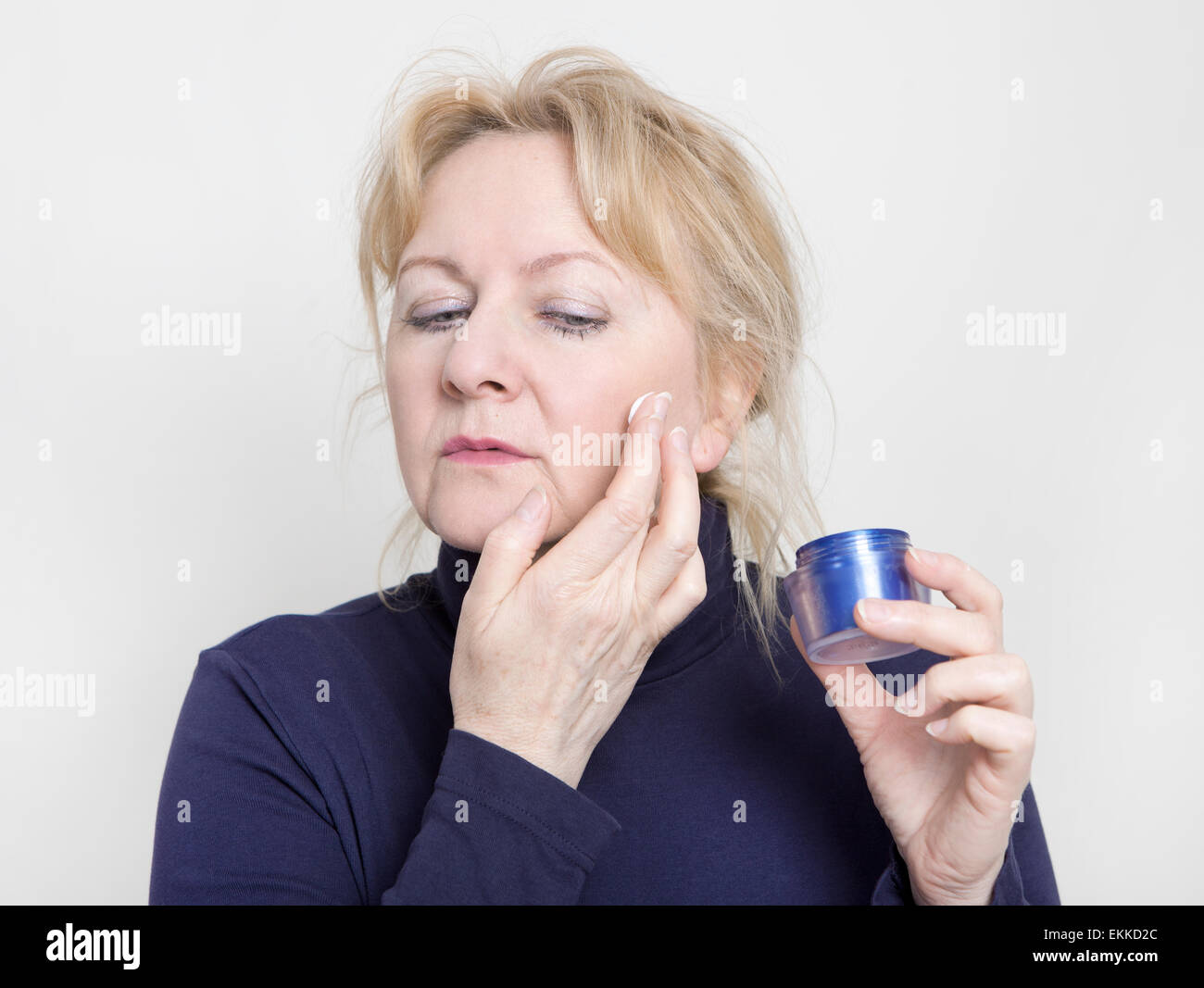 an elderly woman treats her skin on the face with a cream Stock Photo