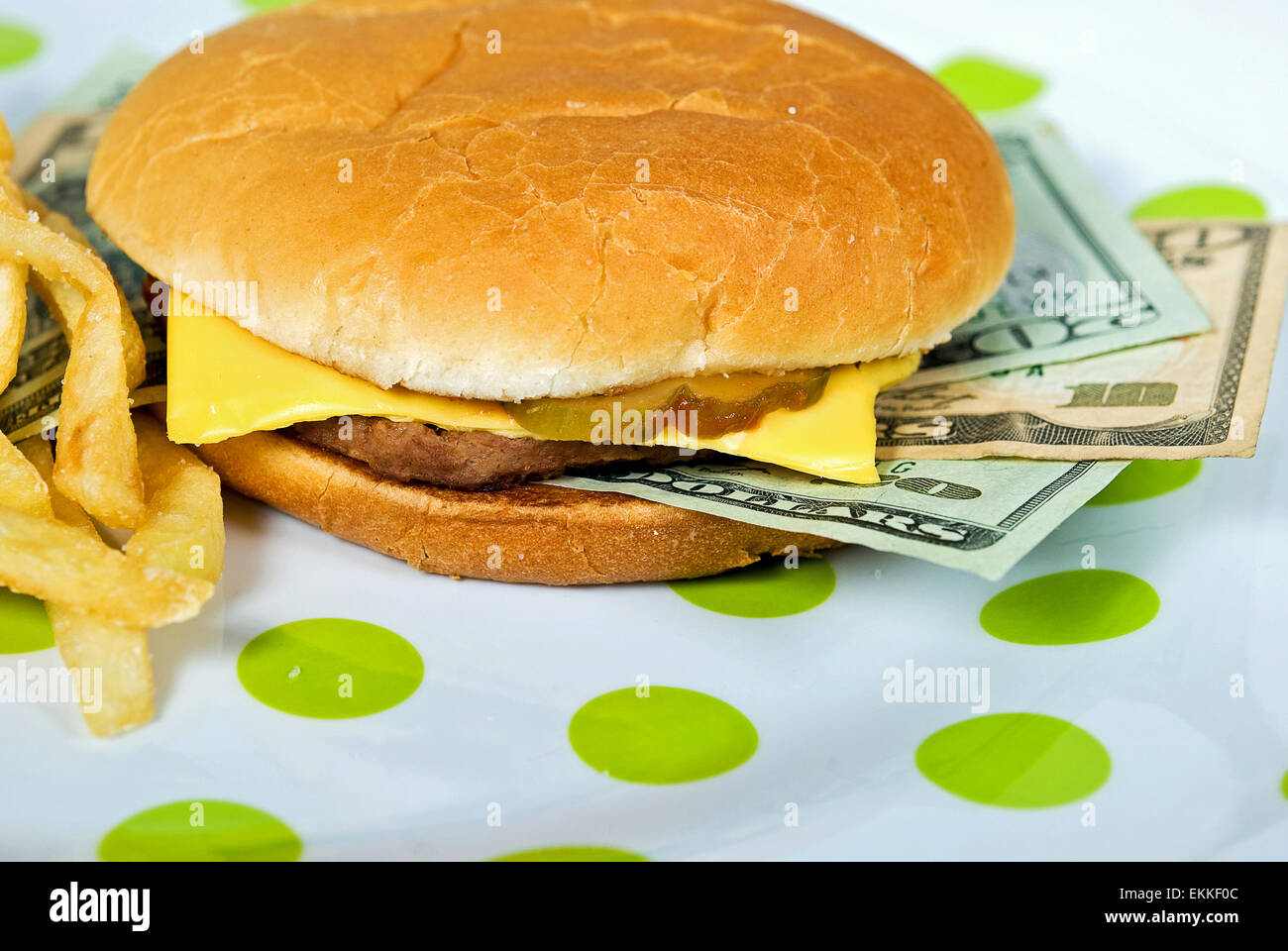 American money in a cheeseburger on a green polka dot plate. Stock Photo