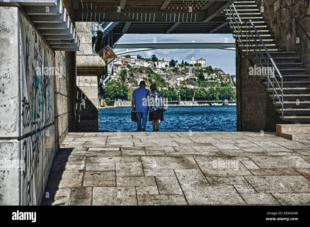 An old couple walk hand in hand under the iron brigde of Oporto, Portugal Stock Photo