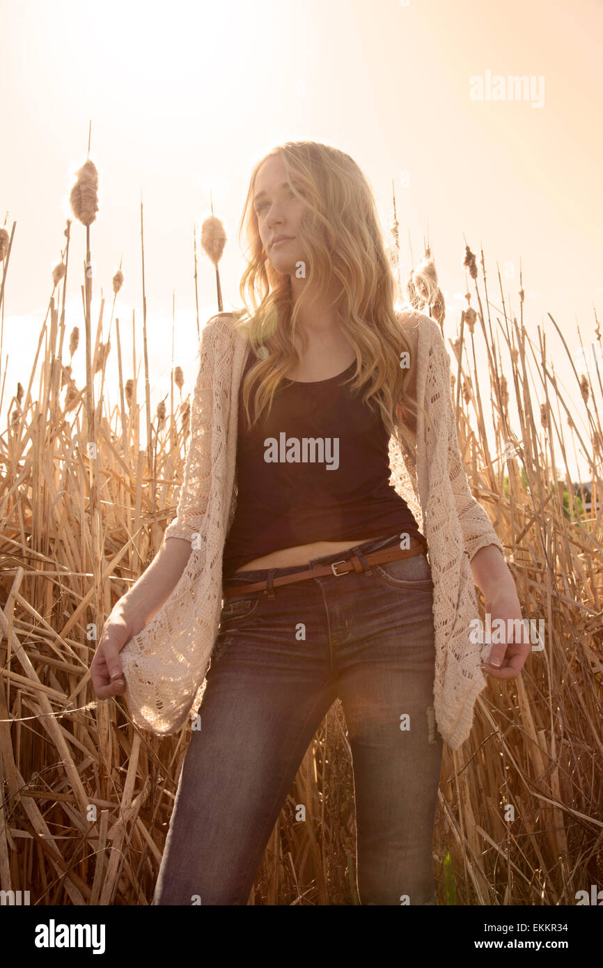 Low angle, outdoor photo of pretty young woman standing in dry grass, backlit, low contrast with warm hues. Stock Photo