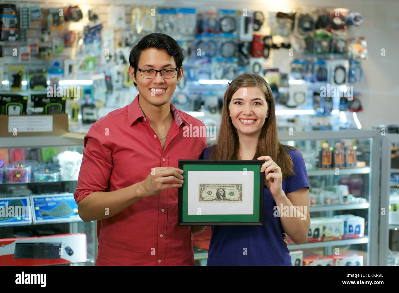 People running small family business, with asian shop owner and caucasian wife in computer store, showing their first dollar to Stock Photo