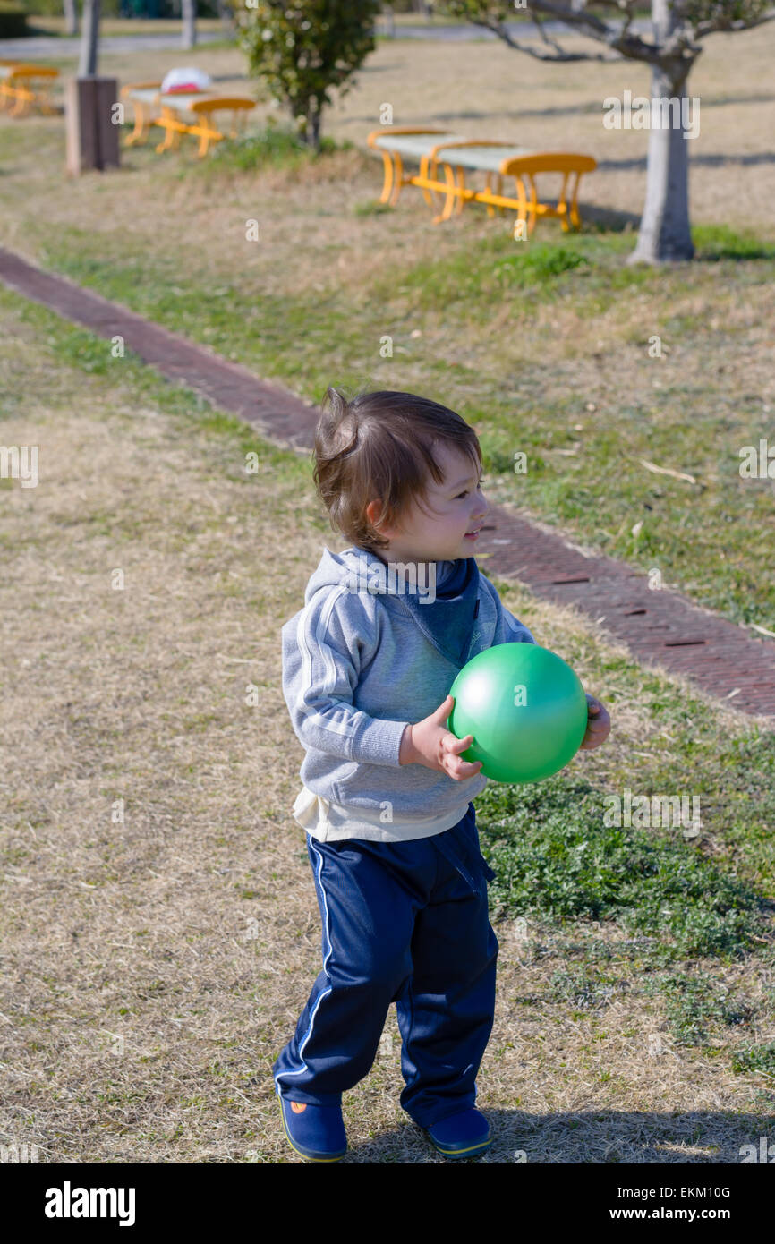 A 2 year old boy holding a ball and smiling at a playground. Stock Photo