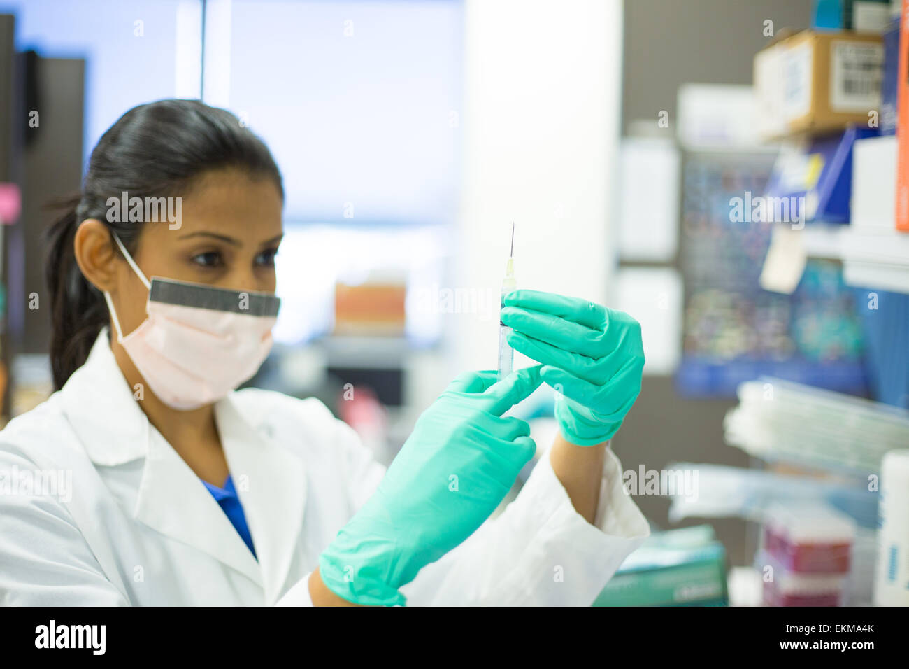 Closeup portrait, smart woman scientist in white labcoat, with face mask, holding syringe needle and flicking,isolated lab Stock Photo