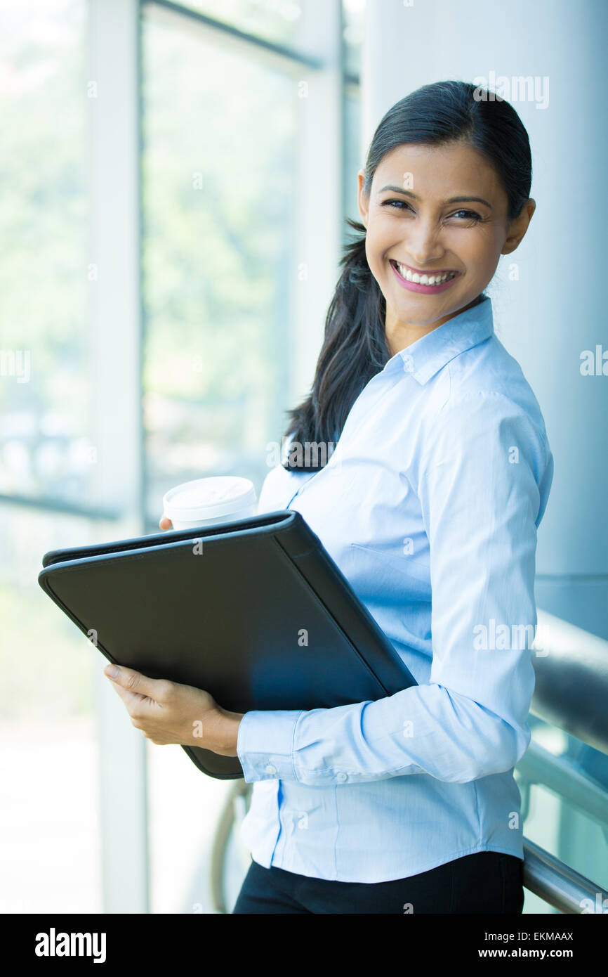 Closeup portrait, young professional, beautiful confident woman in blue shirt, holding coffee and black notebook Stock Photo