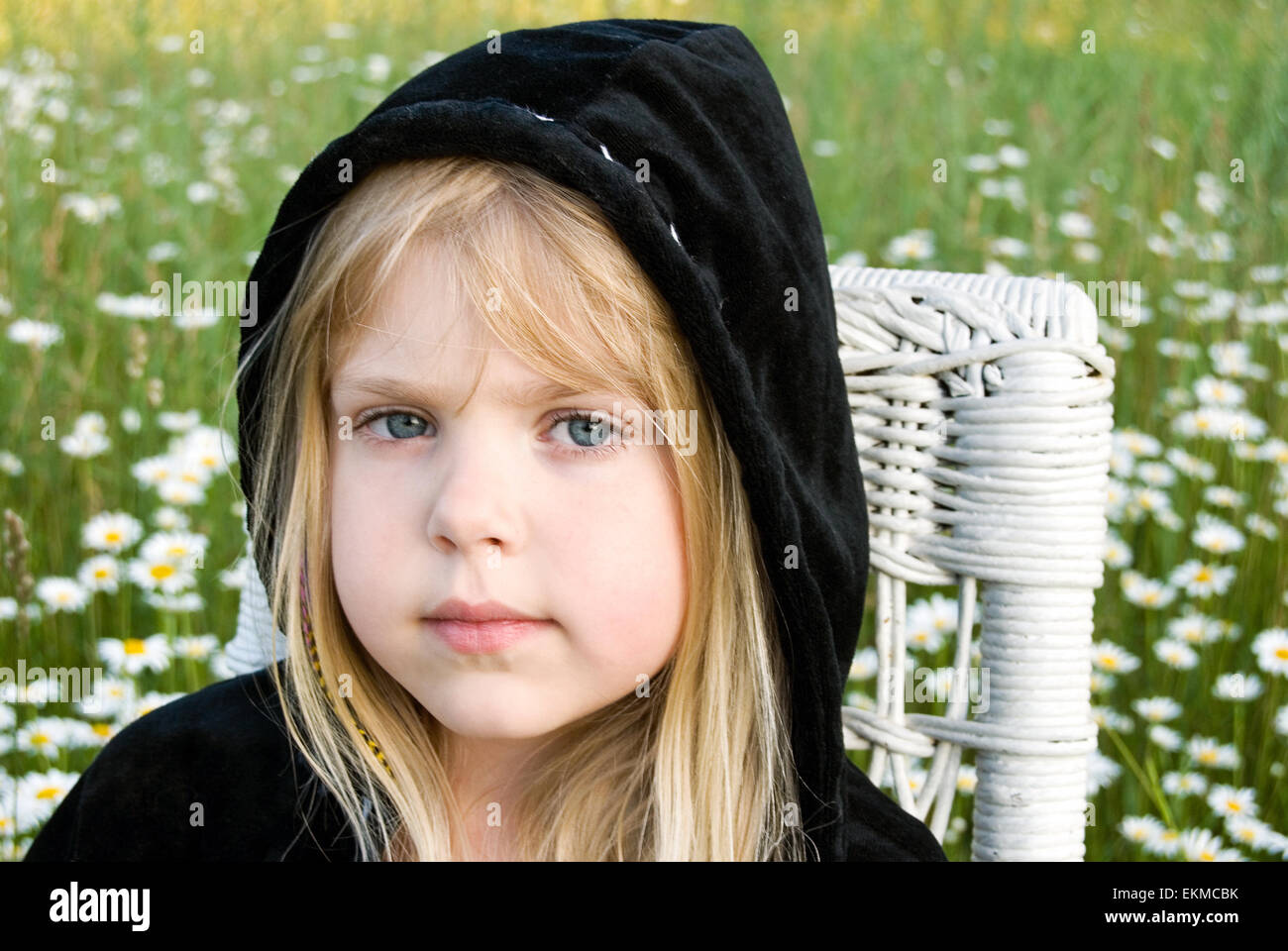 Little blond girl wearing a black velvet hoodie in a white daisy field