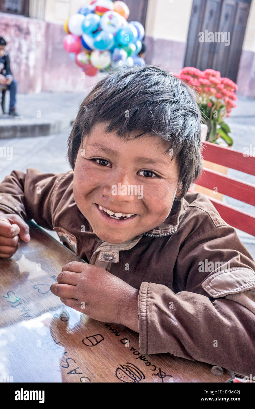 mischievous small indigenous Mexican Indian boy child street vendor approaches table of touriists San Cristobal de las Casas Stock Photo